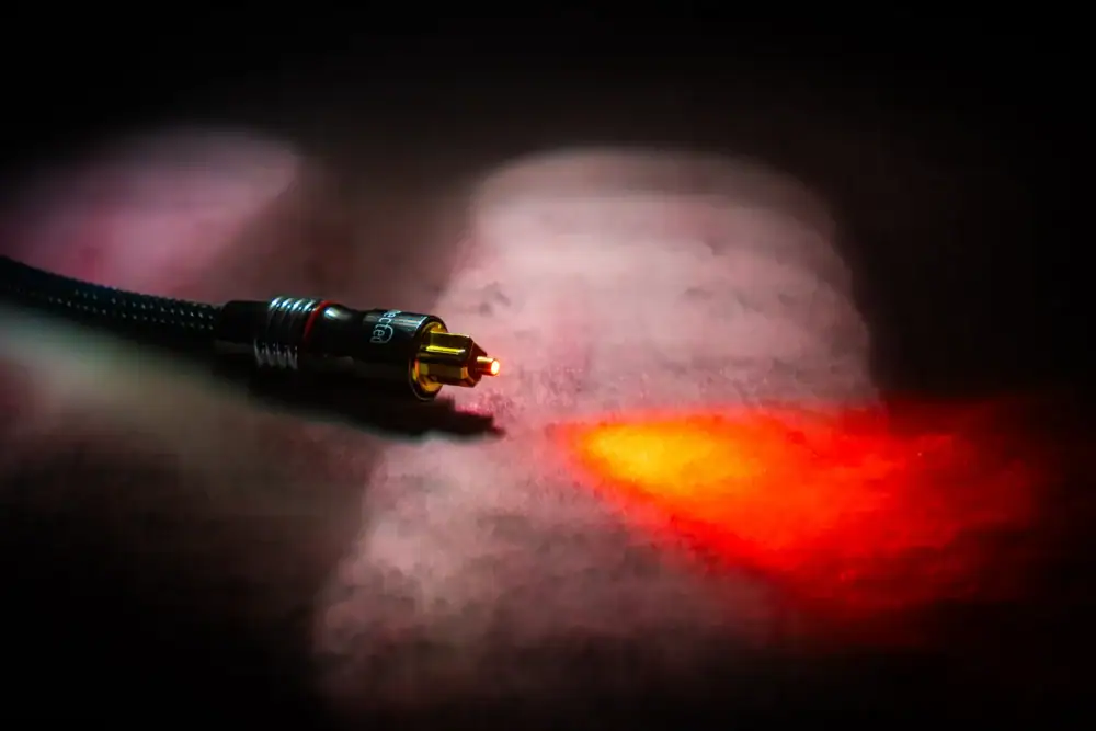 Rood licht uit de connector van een optische kabel in rook: het geluid gaat als licht door de vezel.