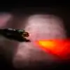 Rood licht uit de connector van een optische kabel in rook: het geluid gaat als licht door de vezel.